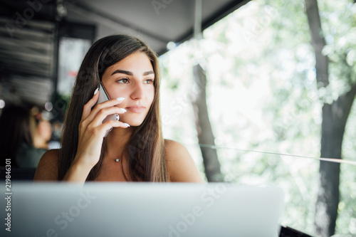 Young beauty woman talking on the phone with a laptop on table in cafe