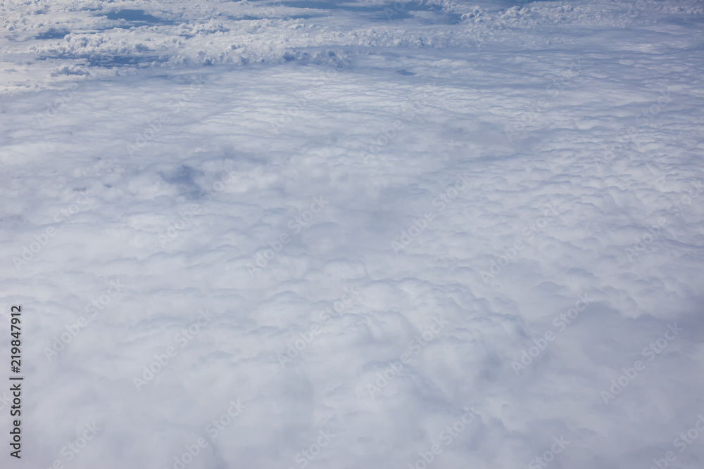 Airplain window seat view of big white thick fluffy clouds with a clear blue sky at the background Airplain window seat view of big white thick fluffy clouds with a clear blue sky at the background