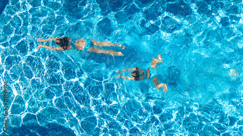 Aerial top view of girls in swimming pool water from above, active children swim, kids have fun on tropical family vacation, holiday resort concept 
