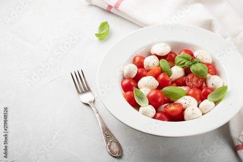 White plate of classic delicious caprese salad with ripe tomatoes, mozzarella and fresh basil leaves on gray background with copy space. Italian food. The concept of a healthy vegetarian diet