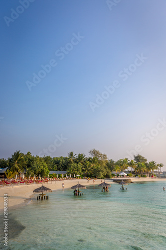 Maldives, Feb 8th 2018 - Tourists enjoying the swimming pool area and the beach area of a resort in Maldives, afternoon lights, some trees and table.