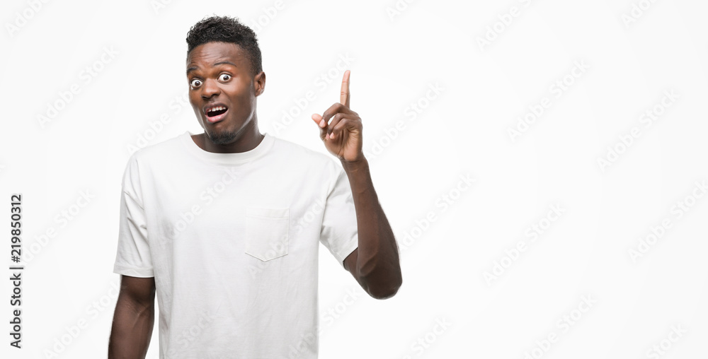 Young african american man wearing white t-shirt pointing finger up with successful idea. Exited and happy. Number one. Young african american man wearing white t-shirt pointing finger up with successful idea. Exited and happy. Number one.