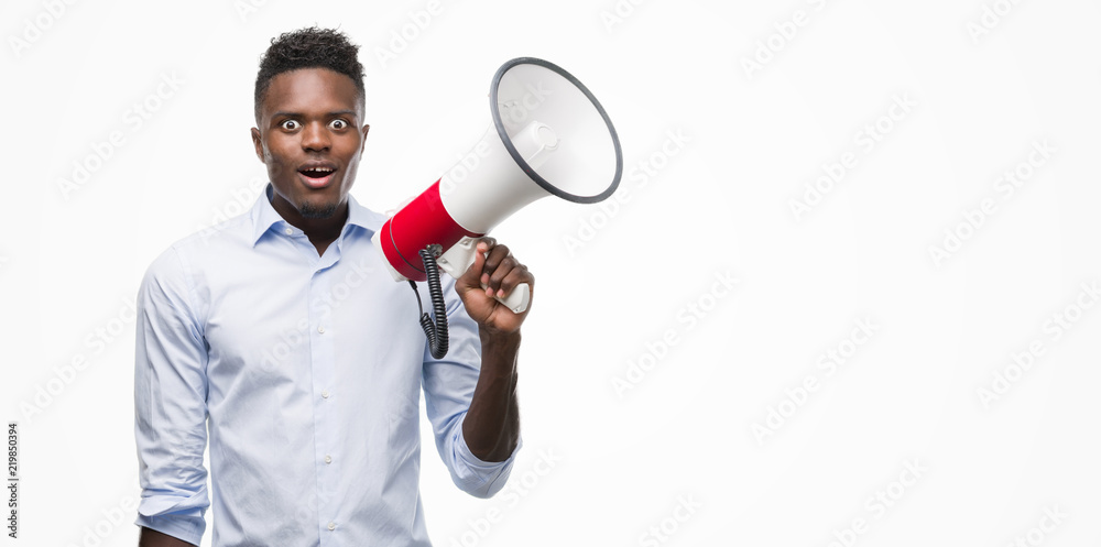Young african american man holding megaphone scared in shock with a surprise face, afraid and excited with fear expression Young african american man holding megaphone scared in shock with a surprise face, afraid and excited with fear expression