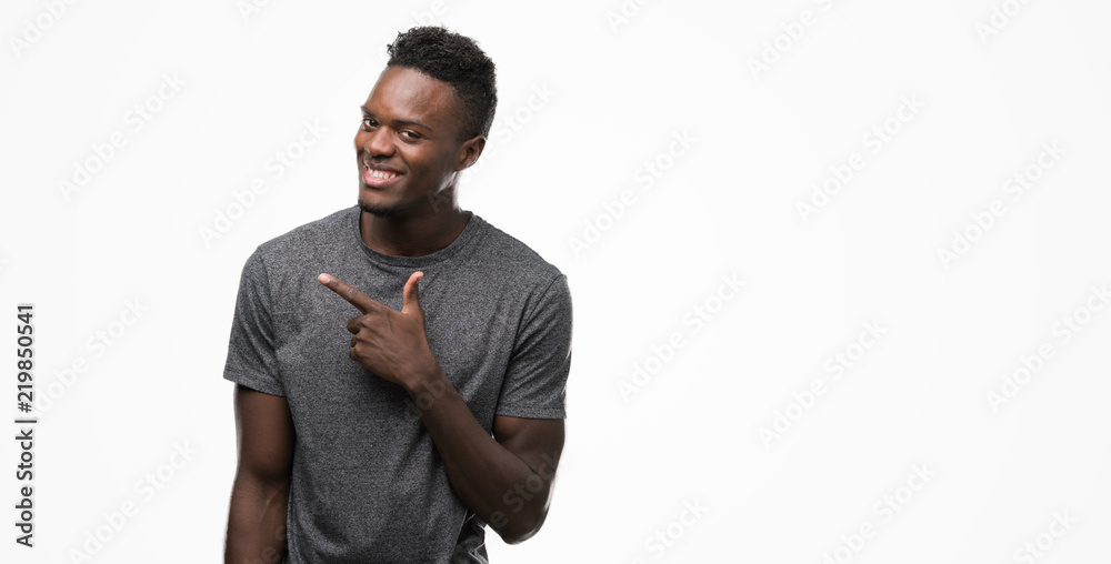 Young african american man wearing grey t-shirt cheerful with a smile of face pointing with hand and finger up to the side with happy and natural expression on face looking at the camera.