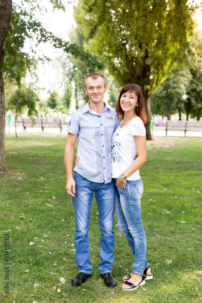 man and woman standing on the lawn. in a white t-shirt and jeans. a walk in the Park. lover. young couple. summer. family. girl and guy . couple smiles man and woman standing on the lawn. in a white t-shirt and jeans. a walk in the Park. lover. young couple. summer. family. girl and guy . couple smiles