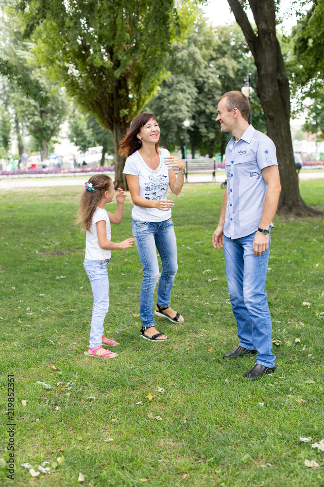 Fototapeta premium daughter mom and dad sitting on the lawn. in a white t-shirt and jeans. a walk in the Park. child. mom dad daughter. summer. family.