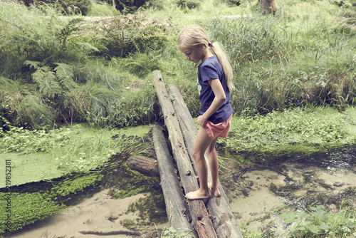 Child cute blond girl playing in the creek. Girl walking in forest stream and exploring nature. Summer children fun. Children summer activities
