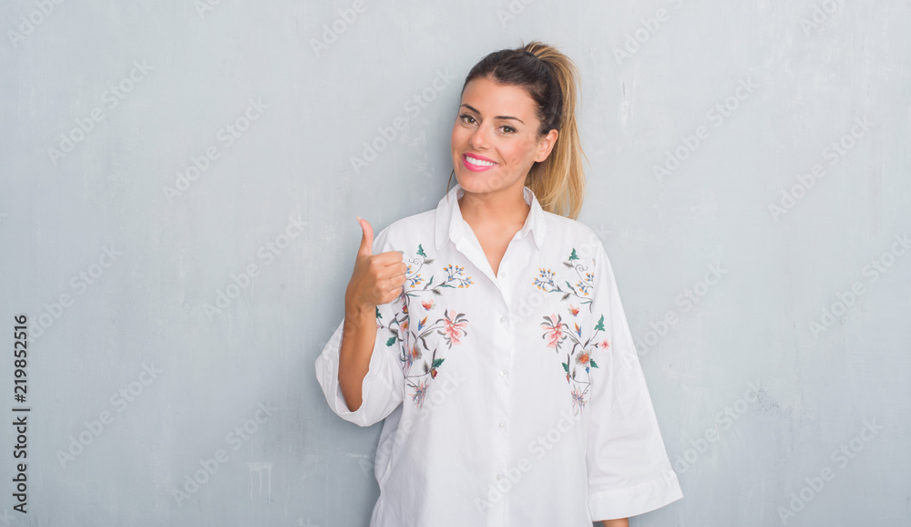 Young adult woman over grunge grey wall wearing flowers shirt doing happy thumbs up gesture with hand. Approving expression looking at the camera with showing success. Young adult woman over grunge grey wall wearing flowers shirt doing happy thumbs up gesture with hand. Approving expression looking at the camera with showing success.