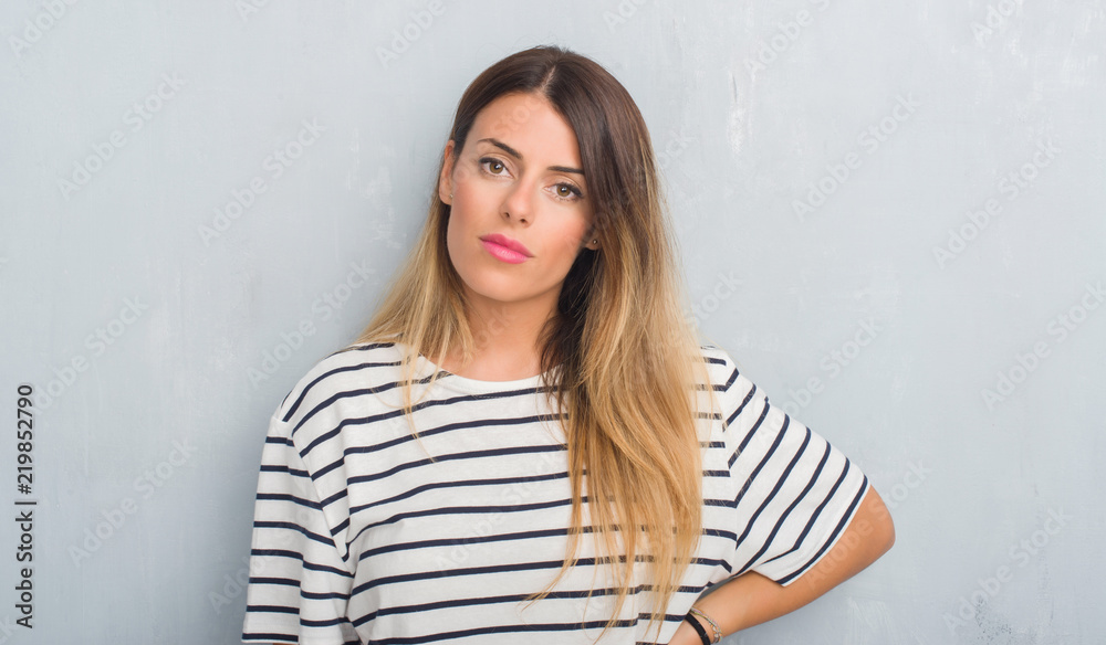Young adult woman over grunge grey wall wearing navy t-shirt with serious expression on face. Simple and natural looking at the camera.