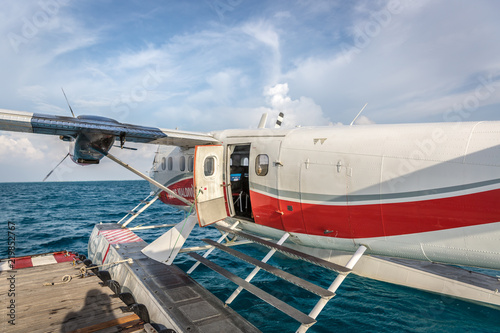 Maldives, Feb 10th 2018 - A seaplane floating in the blue water of Maldives, close to a wood deck with some clouds in the sky.