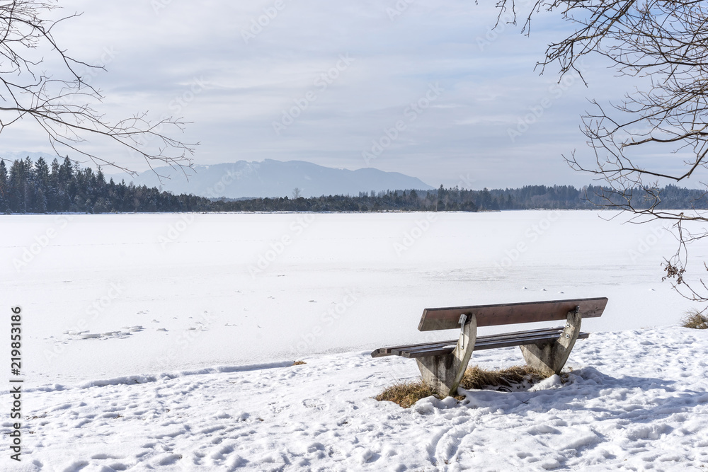 Bench at the frozen Kirchsee lake, Bavaria, with Alps in background, in winter Bench at the frozen Kirchsee lake, Bavaria, with Alps in background, in winter