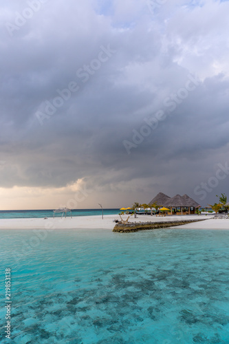 An idyllic island in Maldive in a stormy weather afternoon. Super clear water, white sand, traditional huts and tropical climate feeling. © LMspencer