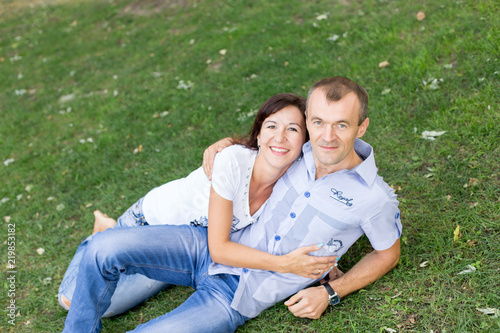 man and woman sitting on the lawn. in a white t-shirt and jeans. a walk in the Park. lover. young couple. summer. family.  embrace