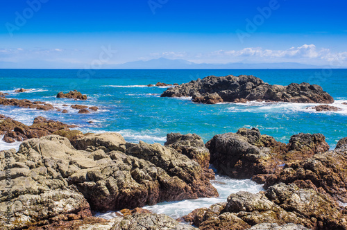 Beautiful view of beach with rock formations in the ocean with waves approaching and blue sky near sand and forest © Fotos 593