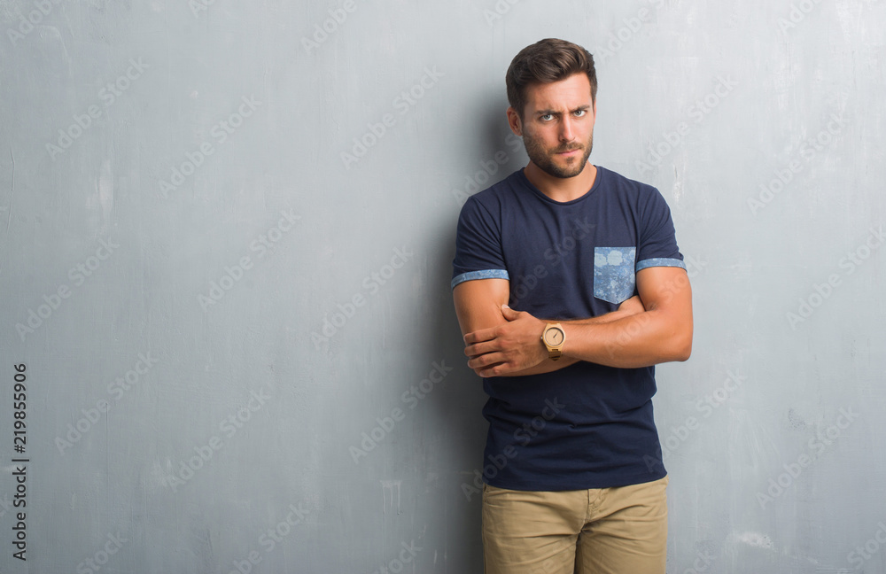 Handsome young man over grey grunge wall skeptic and nervous, disapproving expression on face with crossed arms. Negative person. Handsome young man over grey grunge wall skeptic and nervous, disapproving expression on face with crossed arms. Negative person.