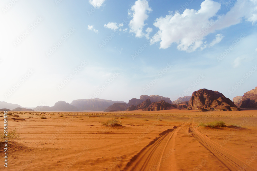 Wadi Rum desert, Jordan, Middle East, known as The Valley of the Moon.  Orange sand, blue sky, haze and clouds. Designation as a UNESCO World Heritage Site. Red planet Mars landscape.