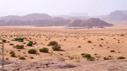 Wadi Rum desert, Jordan, Middle East, The Valley of the Moon. Orange sand, haze, clouds. Designation as a UNESCO World Heritage Site. Red planet Mars landscape. Offroad adventures travel background.