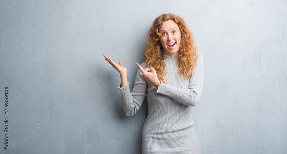 Young redhead woman over grey grunge wall very happy pointing with hand and finger Young redhead woman over grey grunge wall very happy pointing with hand and finger