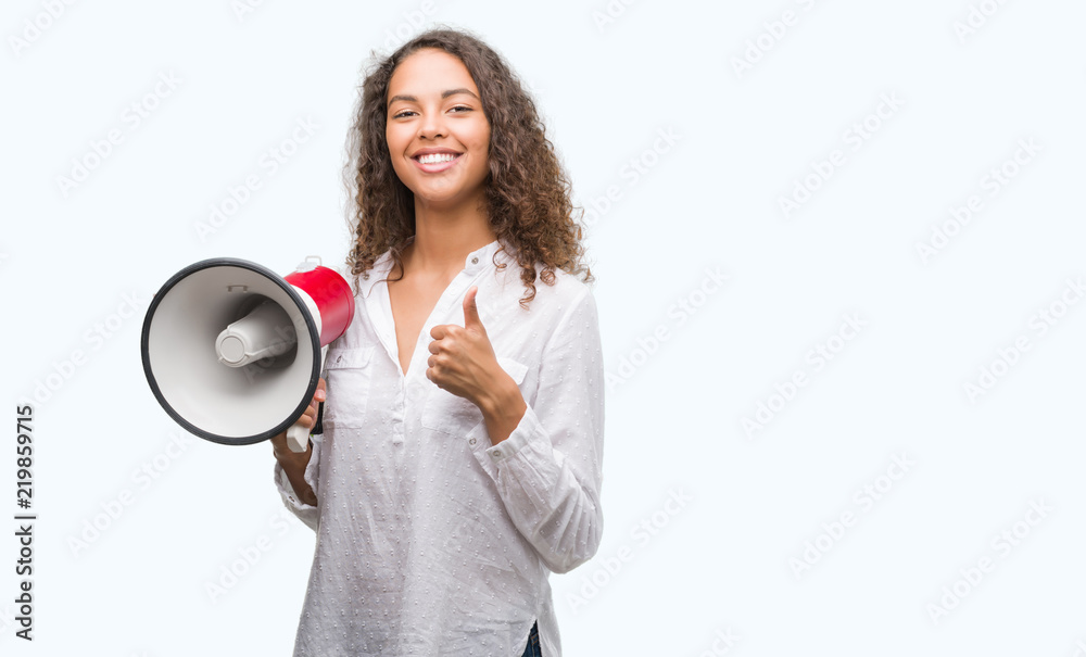 Young hispanic woman holding megaphone happy with big smile doing ok sign, thumb up with fingers, excellent sign Young hispanic woman holding megaphone happy with big smile doing ok sign, thumb up with fingers, excellent sign