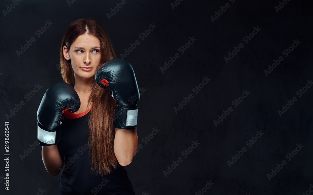 Sportive woman dressed in sportswear wearing boxing gloves posing in a studio. Isolated on a dark textured background.