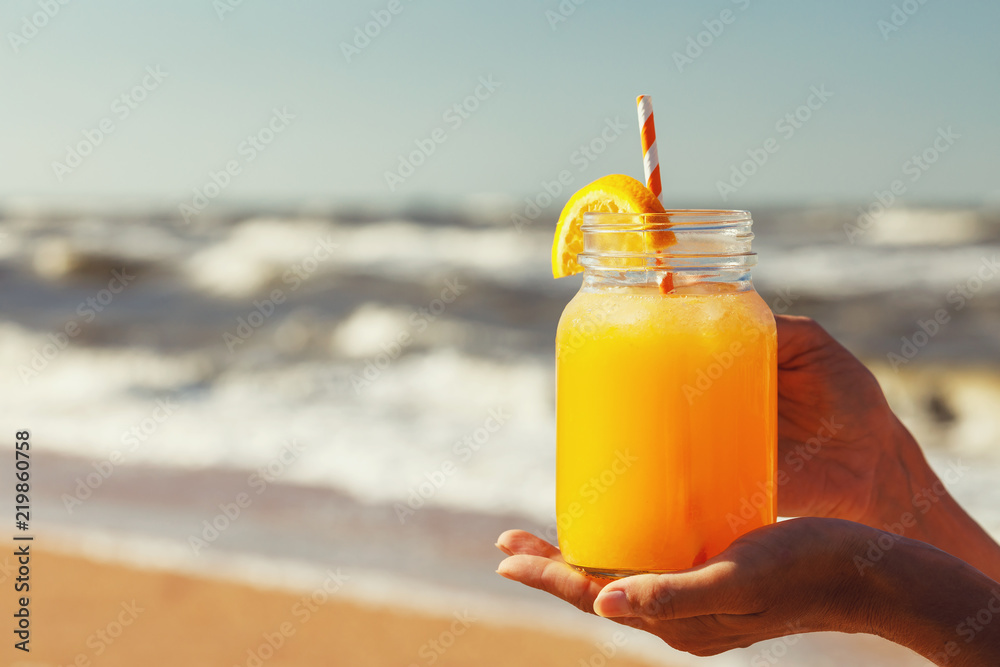 Orange juice with pulp in hands on the beach with space for text
