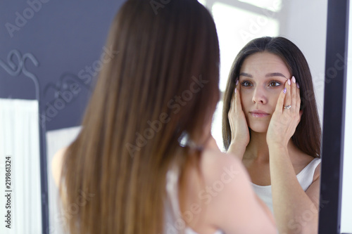 Young woman looking herself reflection in mirror at home.