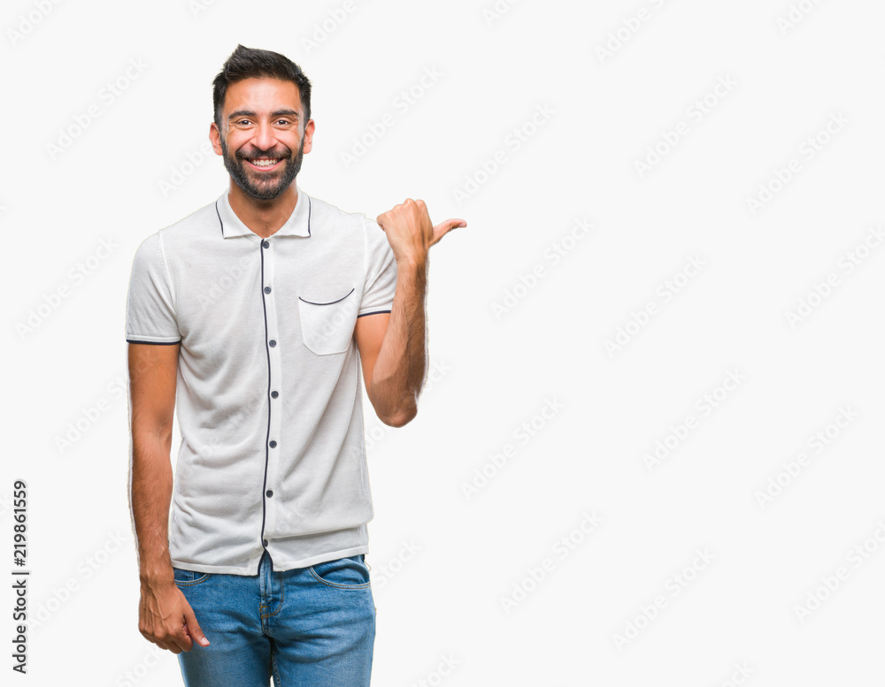 Adult hispanic man over isolated background smiling with happy face looking and pointing to the side with thumb up. Adult hispanic man over isolated background smiling with happy face looking and pointing to the side with thumb up.
