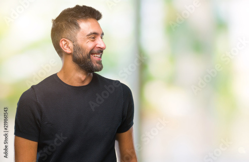Adult hispanic man over isolated background looking away to side with smile on face, natural expression. Laughing confident.