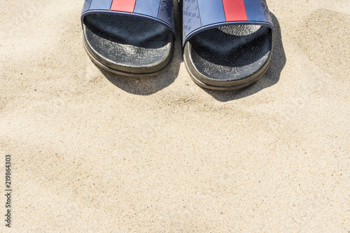 blue flip flops with black soles slapping on the beach with fine sand, vacation abstract background, summer sunny day