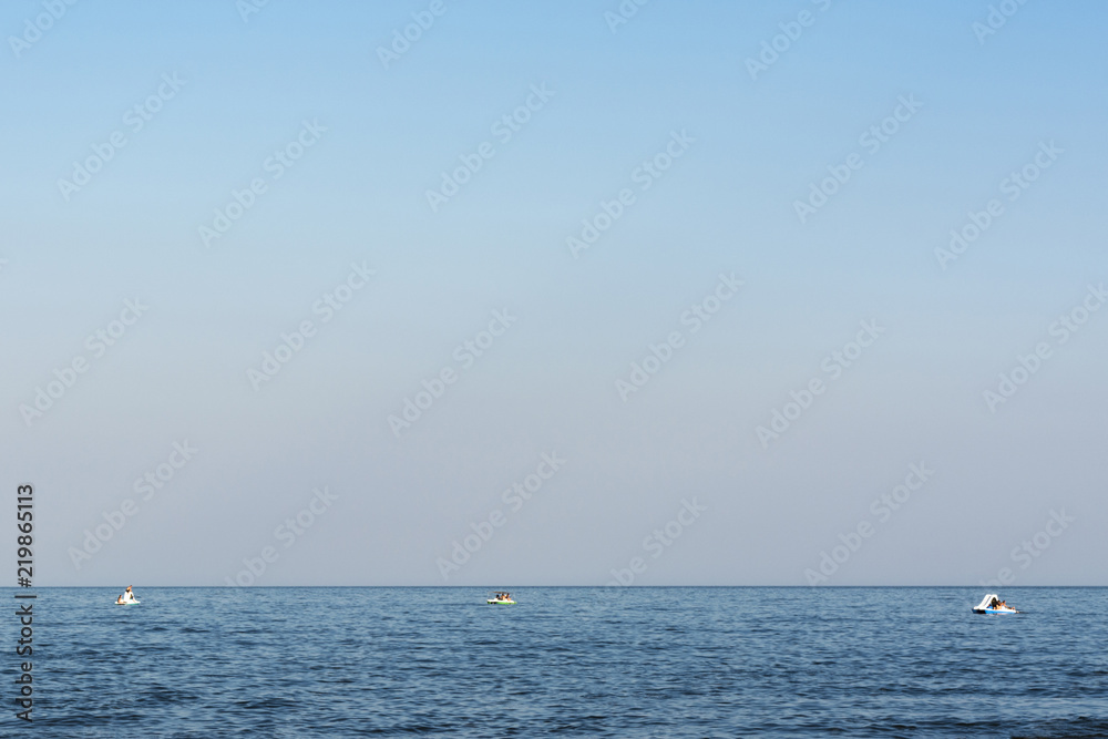 blue sea with waves, far away on a horizon line floating three catamarans with people