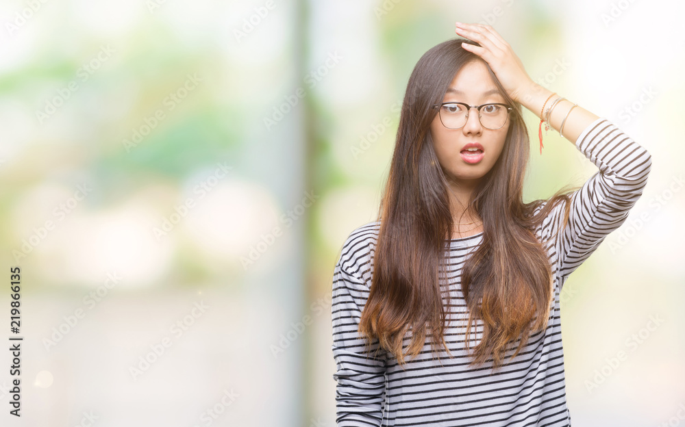 Young asian woman wearing glasses over isolated background surprised with hand on head for mistake, remember error. Forgot, bad memory concept.