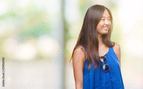 Young asian woman over isolated background looking away to side with smile on face, natural expression. Laughing confident.