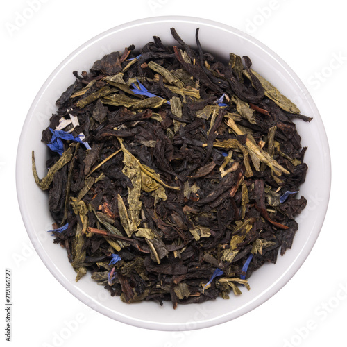 Mix of black tea with green sencha tea and cornflower flowers and strawberry slices in white bowl on white background
