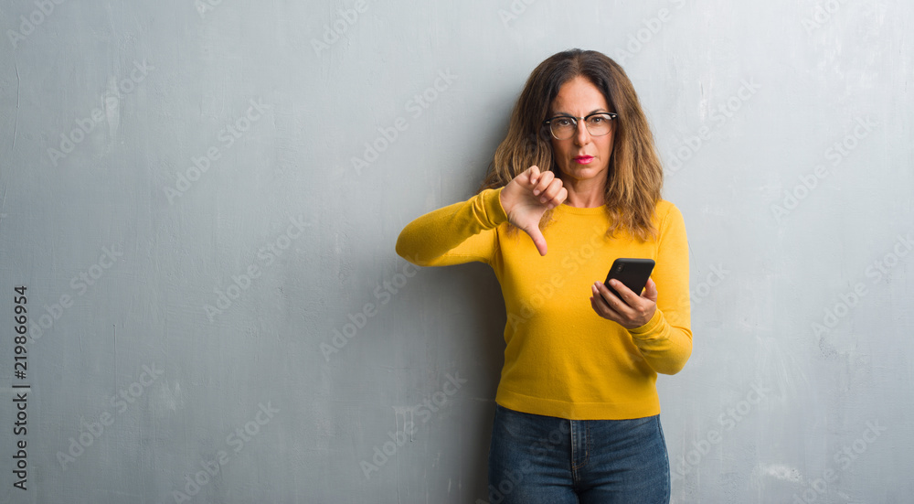 Middle age hispanic woman using smartphone with angry face, negative sign showing dislike with thumbs down, rejection concept Middle age hispanic woman using smartphone with angry face, negative sign showing dislike with thumbs down, rejection concept