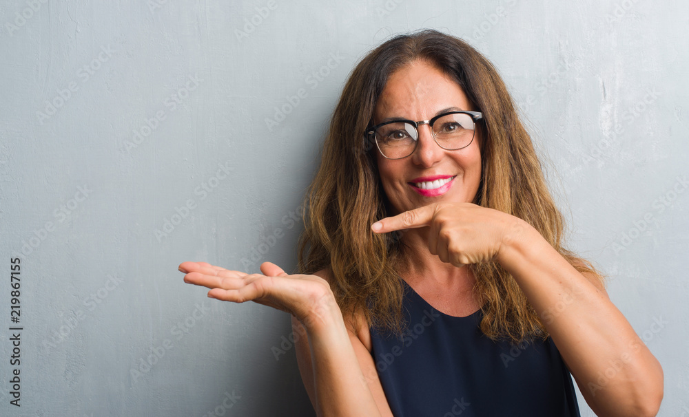 Fototapeta premium Middle age hispanic woman over grey wall wearing glasses very happy pointing with hand and finger