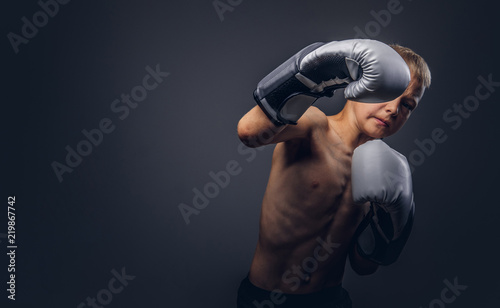 Shirtless young boxer with blonde hair wearing boxing gloves shows a boxing hook.