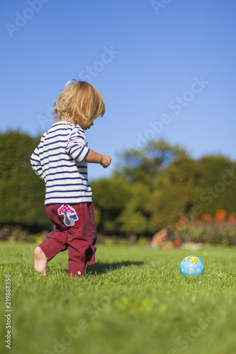 Kind spielt mit kleinem Ball Fußball in Wiese. Child playing with little ball football in park. 