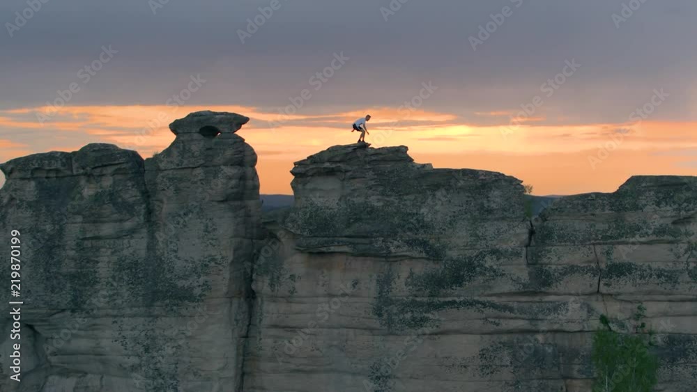 Side view of sportive anonymous man running and jumping extremely on top of long cliff against sunset sky