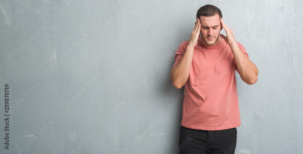 Young caucasian man over grey grunge wall with hand on head for pain in head because stress. Suffering migraine. Young caucasian man over grey grunge wall with hand on head for pain in head because stress. Suffering migraine.