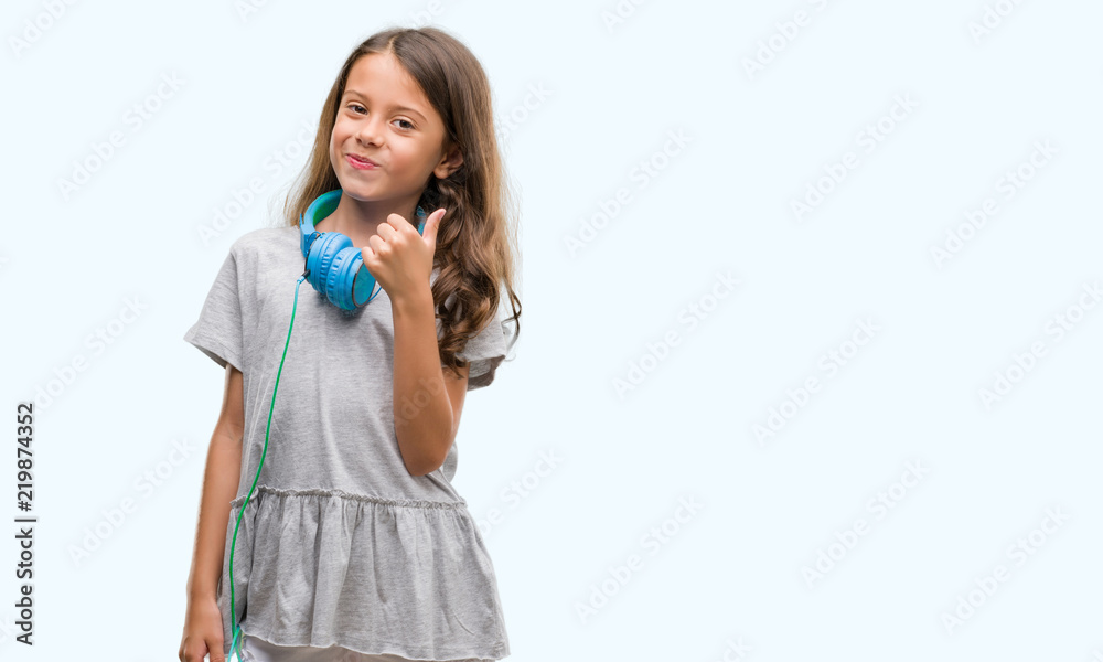 Brunette hispanic girl wearing headphones happy with big smile doing ok sign, thumb up with fingers, excellent sign Brunette hispanic girl wearing headphones happy with big smile doing ok sign, thumb up with fingers, excellent sign