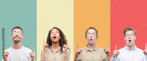 Collage of a group of people isolated over colorful background amazed and surprised looking up and pointing with fingers and raised arms.