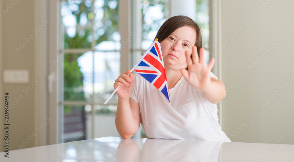 Down syndrome woman at home holding flag of uk with open hand doing stop sign with serious and confident expression, defense gesture
