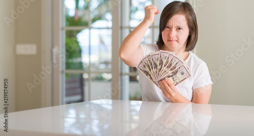 Down syndrome woman at home holding dollars annoyed and frustrated shouting with anger, crazy and yelling with raised hand, anger concept © Krakenimages.com