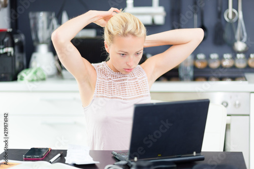 Female freelancer in her casual home clothing working remotly from her dining table in the morning. Home kitchen in the background. photo