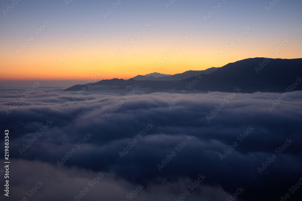 Yuanyang County - Yunnan Province, China. Dawn, Sunrise panoramic view, sea of clouds with an orange glow behind a mountain silhouette. Above the clouds, silhouette, mountain background, red horizon
