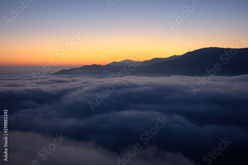 Yuanyang County - Yunnan Province, China. Dawn, Sunrise panoramic view, sea of clouds with an orange glow behind a mountain silhouette. Above the clouds, silhouette, mountain background, red horizon © Cedar