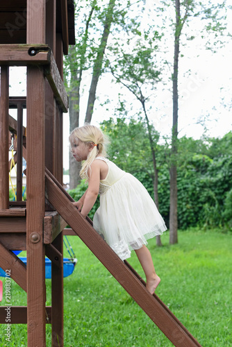 Fényképezés Little girl climbing swingset ladder in a dress