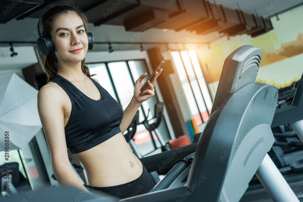 Asian woman exercising in the gym, Young woman workout in fitness for her healthy and office girl lifestyle. She using smart phone to check an email or social network. Asian woman exercising in the gym, Young woman workout in fitness for her healthy and office girl lifestyle. She using smart phone to check an email or social network.