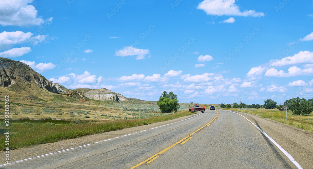 An old cabless harvester travelling along a highway on a sunny afternoon in a rocky Montana countryside
