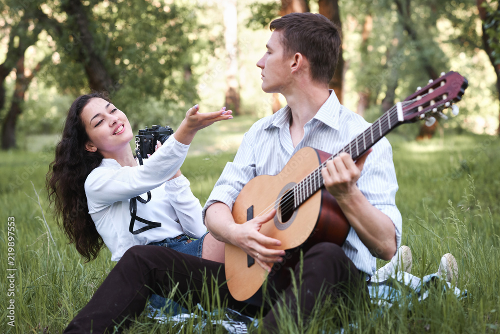 young couple sitting in the forest and playing guitar, taking photo on old camera, summer nature, bright sunlight, shadows and green leaves, romantic feelings young couple sitting in the forest and playing guitar, taking photo on old camera, summer nature, bright sunlight, shadows and green leaves, romantic feelings